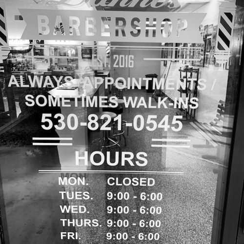 A sign in the window of a barber shop with the words "Open" and "Haircuts Available".